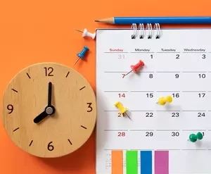 Homem focado organizando sua agenda com um laptop e materiais de estudo em uma mesa limpa, representando produtividade e gestão do tempo.
