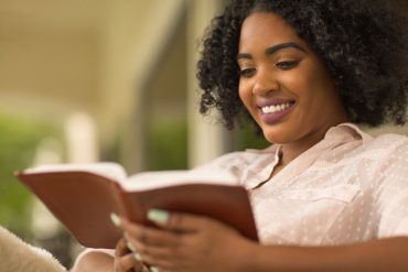 Mulher cristã sorrindo, segurando um livro sobre sexualidade, com fundo de luz suave.