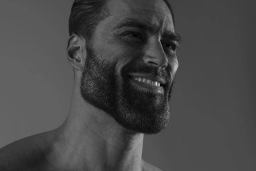 Homem musculoso exibindo abdômen definido, vestindo roupa esportiva, com fundo desfocado de academia moderna.